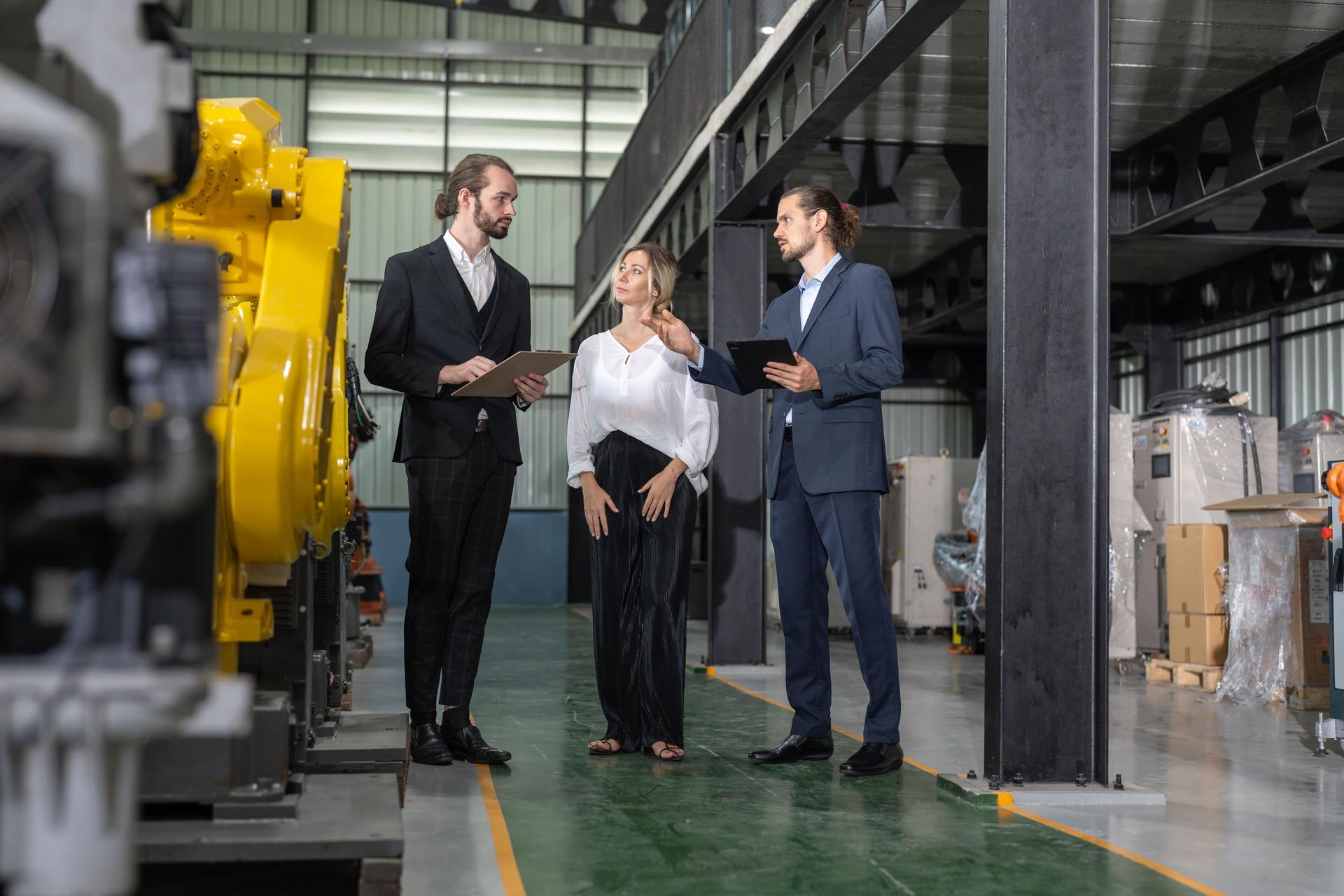 Two businessman visits robot factory. Female owner engineer explaining assembling robot arms welding machine at robotic warehouse factory